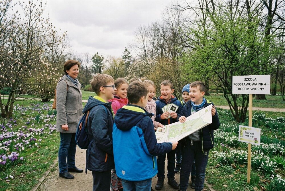 Uczniowie biorą udział w grze terenowej „Tropem wiosny” i szukają wskazówek w parku.