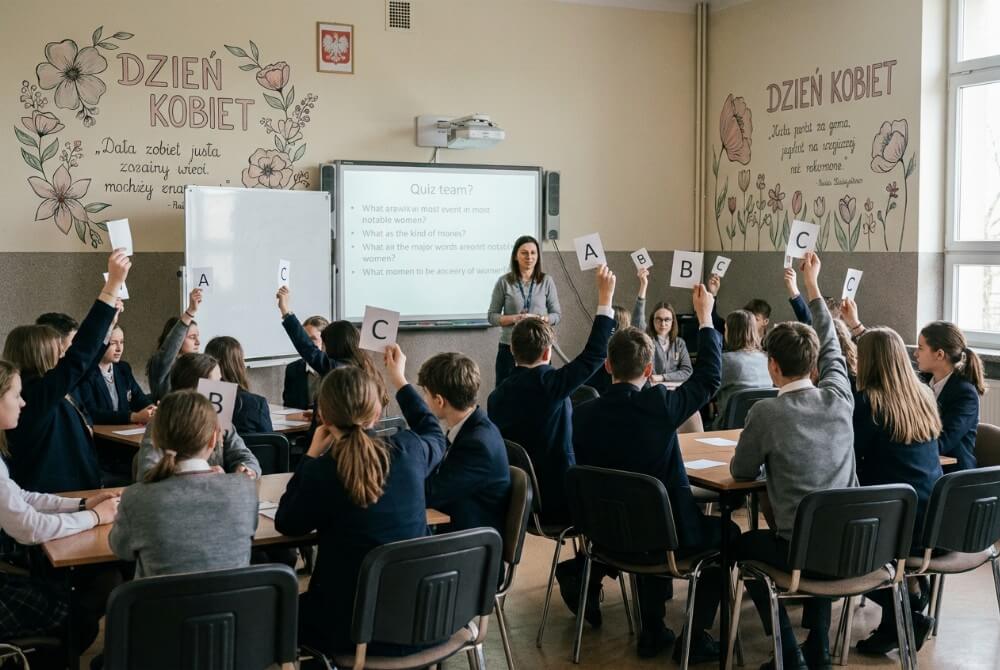 Drużynowy quiz w klasie, uczniowie odpowiadają na pytania, trzymając kartki z odpowiedziami.