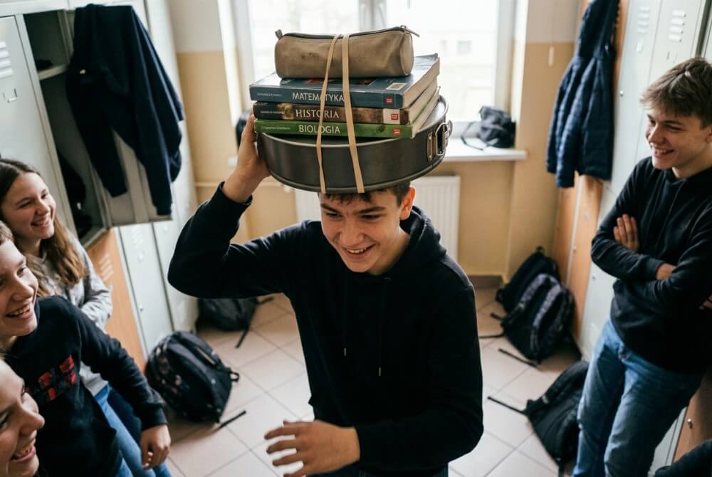 Uczeń niesie zeszyty na tacy do ciasta, balansując ją na głowie w szkole.